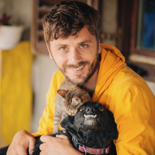 Smiling happy man holding a dog and cat.